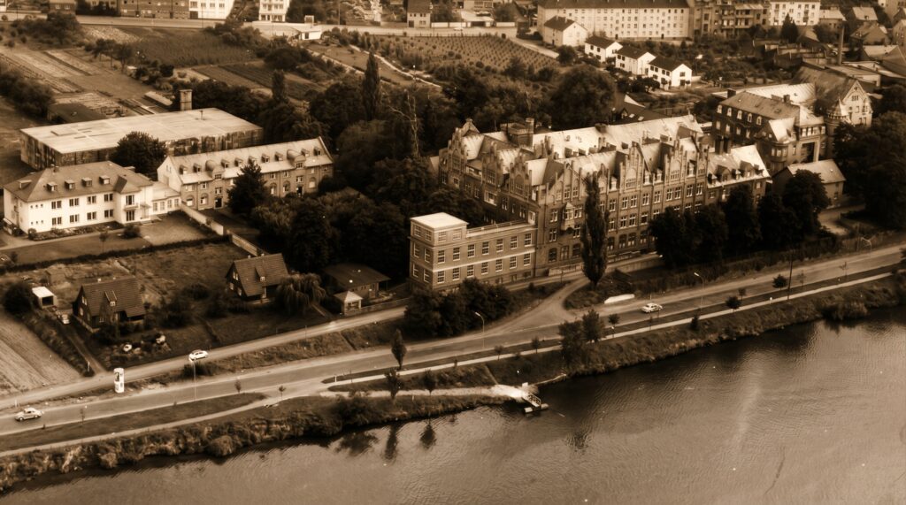 Das Kemperhofgelände Mitte der 1950er-Jahre. Undatierte Postkarte. Vorne der nach Plänen des Architekten Osterhaus errichtete Moselflügel, links daneben der kleine Anbau aus den frühen 1920er-Jahren mit Liegeter-rasse. Am linken Bildrand ist das 1953 eingeweihte „Lungenhaus“ zu sehen, direkt dahinter der Ostbunker. Foto: Stadtarchiv Koblenz.