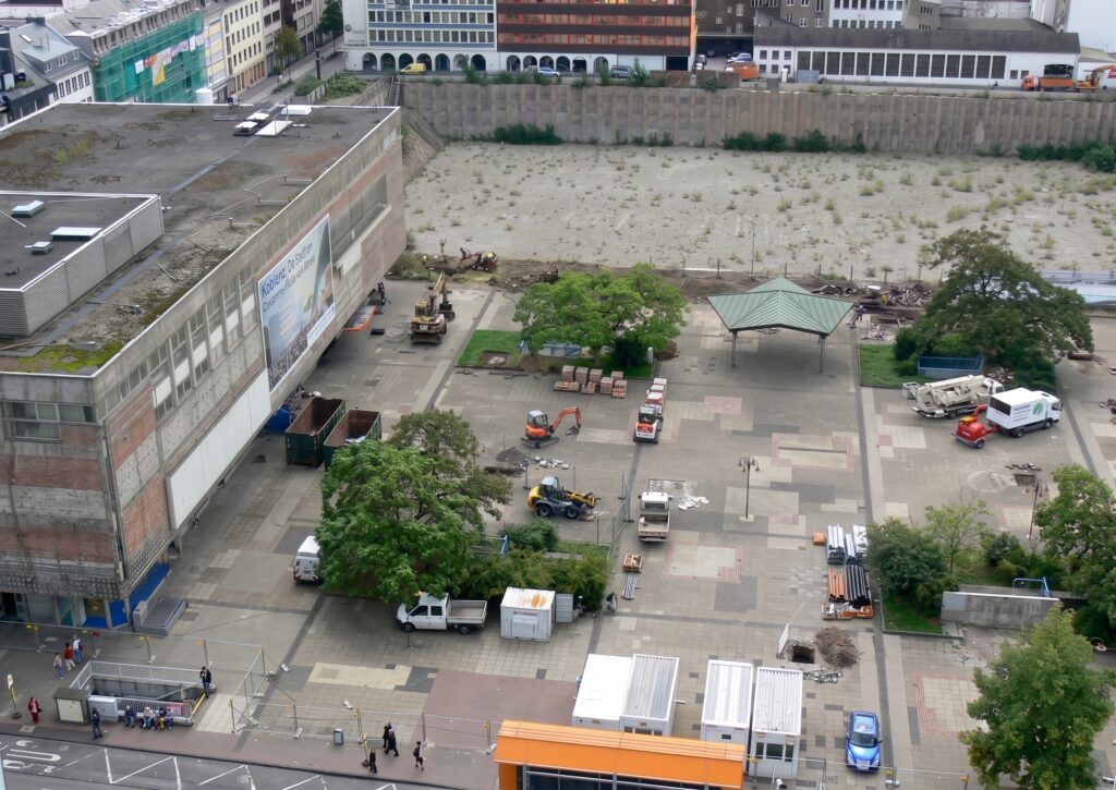 Der im Bereich der mittelalterlichen Wasserturmsmauer entstandene Zentralplatz stand von Anfang an im Mittelpunkt der Kritik am Koblenzer Stadtbild. Es sollte sich schnell herausstellen, dass der in den späten 1960er- und frühen 1970er-Jahren geschaffene Platz nicht so funktionieren würde, wie gedacht. Die Debatten gipfelten mit der Entscheidung für den Bau des Forums Confluentes und des Forums Mittelrhein in den Jahren 2010 bis 2013. Das Foto entstand kurz vor dem Abbruch des Hertie-Gebäudes (früher Quelle).